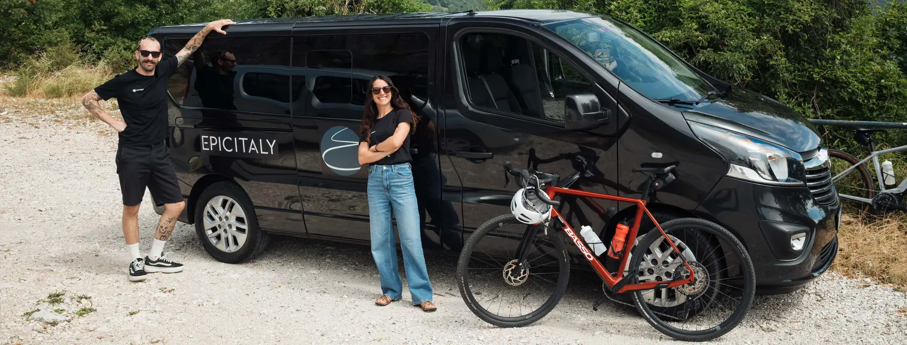Susi and Benji by the Epic Italy van on a hillside road, with a bike leaning against it