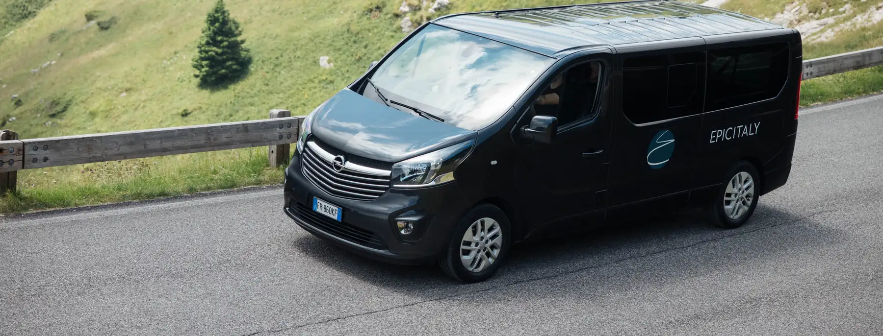 The black Epic Italy van on a quiet mountain road, with green slopes behind