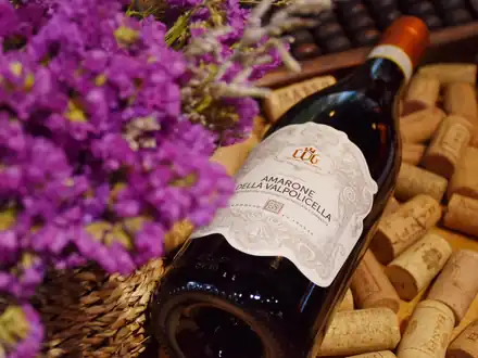 A bottle of Amarone della Valpolicella lying on a bed of corks, with purple flowers beside it