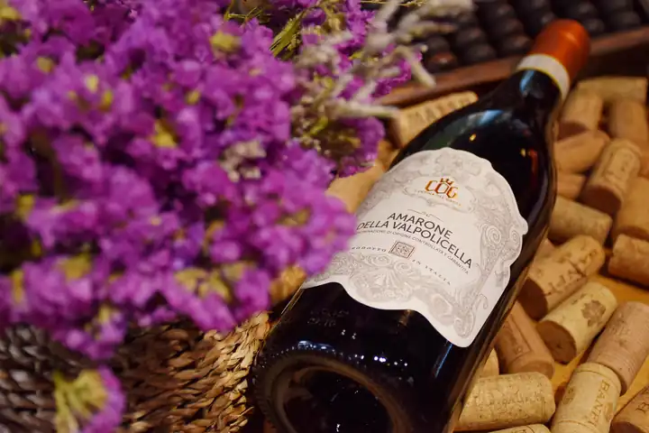 A bottle of Amarone della Valpolicella lying on a bed of corks, with purple flowers beside it