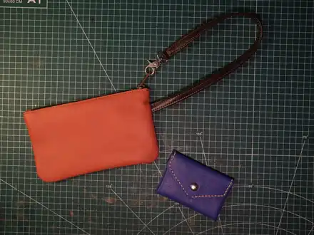 An orange leather pouch and a small purple purse on a cutting mat