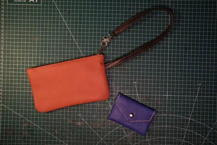 An orange leather pouch and a small purple purse on a cutting mat
