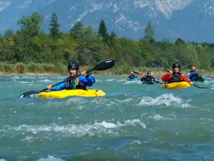 Kayakers paddling through white water on the Brenta, mountains behind