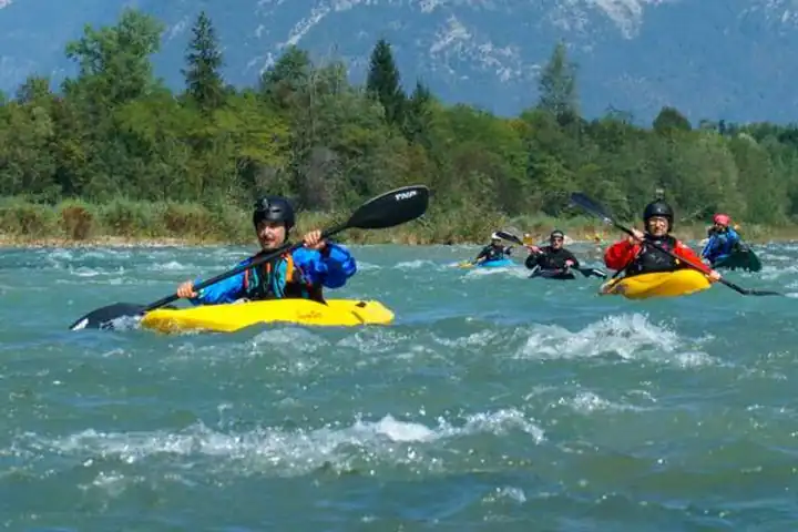 Kayakers paddling through white water on the Brenta, mountains behind