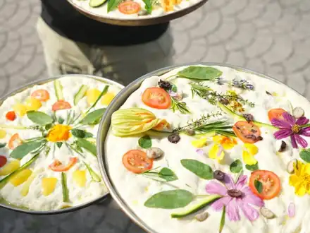 Two focacce decorated with vegetables and edible flowers
