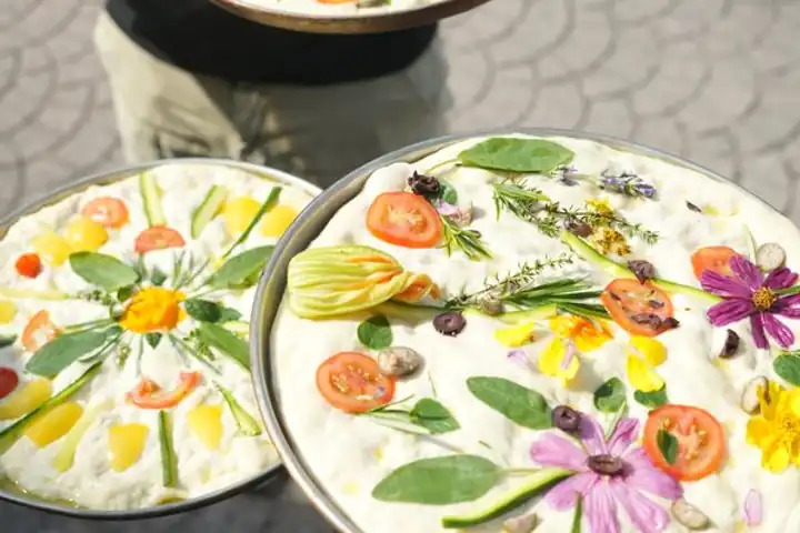Two focacce decorated with vegetables and edible flowers