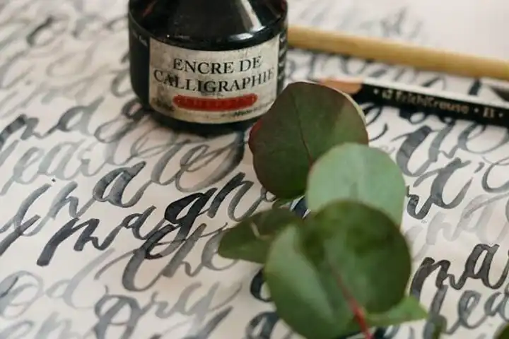 Calligraphy on paper beside a sprig of leaves