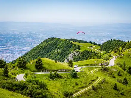 A paraglider above the green slopes of Monte Grappa, with the plain far below
