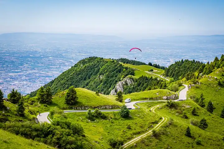 A paraglider above the green slopes of Monte Grappa, with the plain far below
