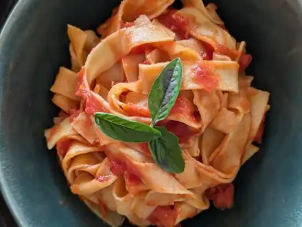 A bowl of fresh tagliatelle with tomato sauce and basil
