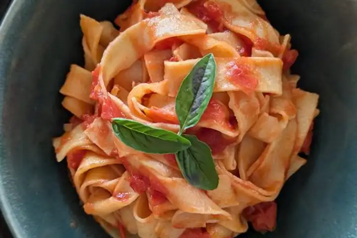 A bowl of fresh tagliatelle with tomato sauce and basil