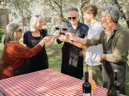 Guests raising glasses of red wine around a table under the olive trees