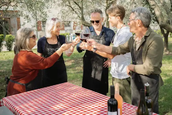 Guests raising glasses of red wine around a table under the olive trees
