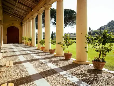 The colonnaded portico of a Palladian villa, with lemon trees in pots along the lawn