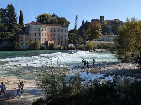 A villa beside the river, with people walking on the stony banks
