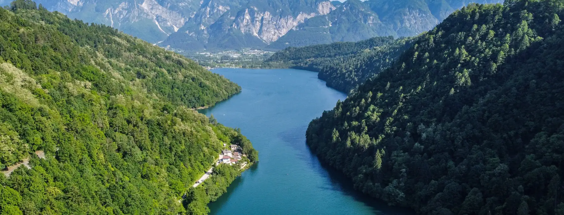 A mountain lake between steep wooded slopes, with the Trentino peaks behind