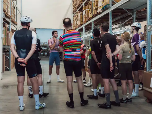 Riders in cycling kit listening to a talk inside the Basso workshop