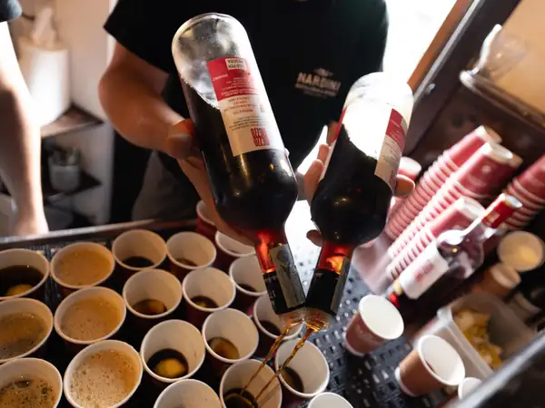 Grappa being poured into rows of small cups at a tasting