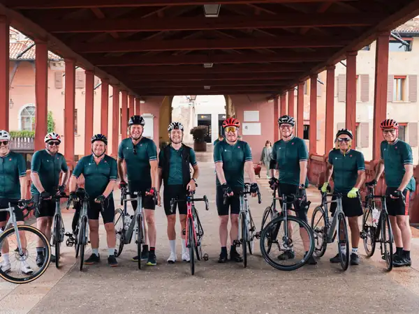 A group of riders in matching kit lined up with their bikes on the Ponte degli Alpini