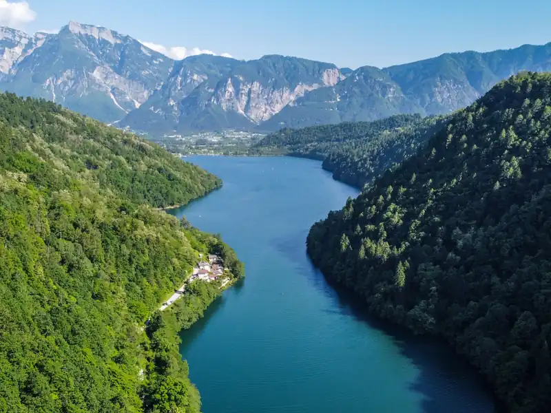 A mountain lake between steep wooded slopes, with the Trentino peaks behind