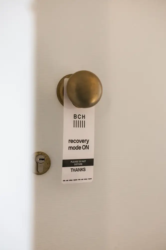 A "recovery mode on" sign hanging on a bedroom door at Bassano Club House (BCH)