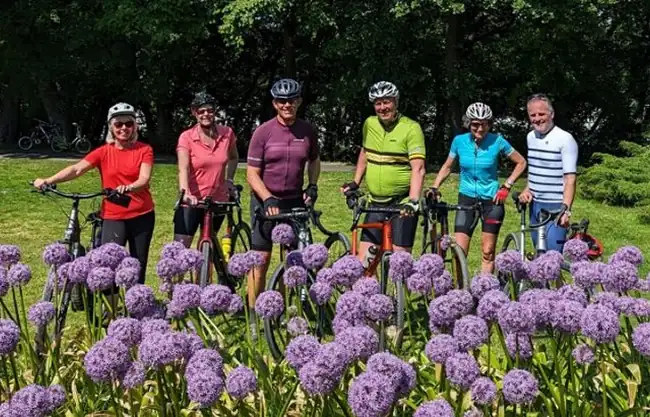 Six riders with their bikes behind a bed of purple alliums