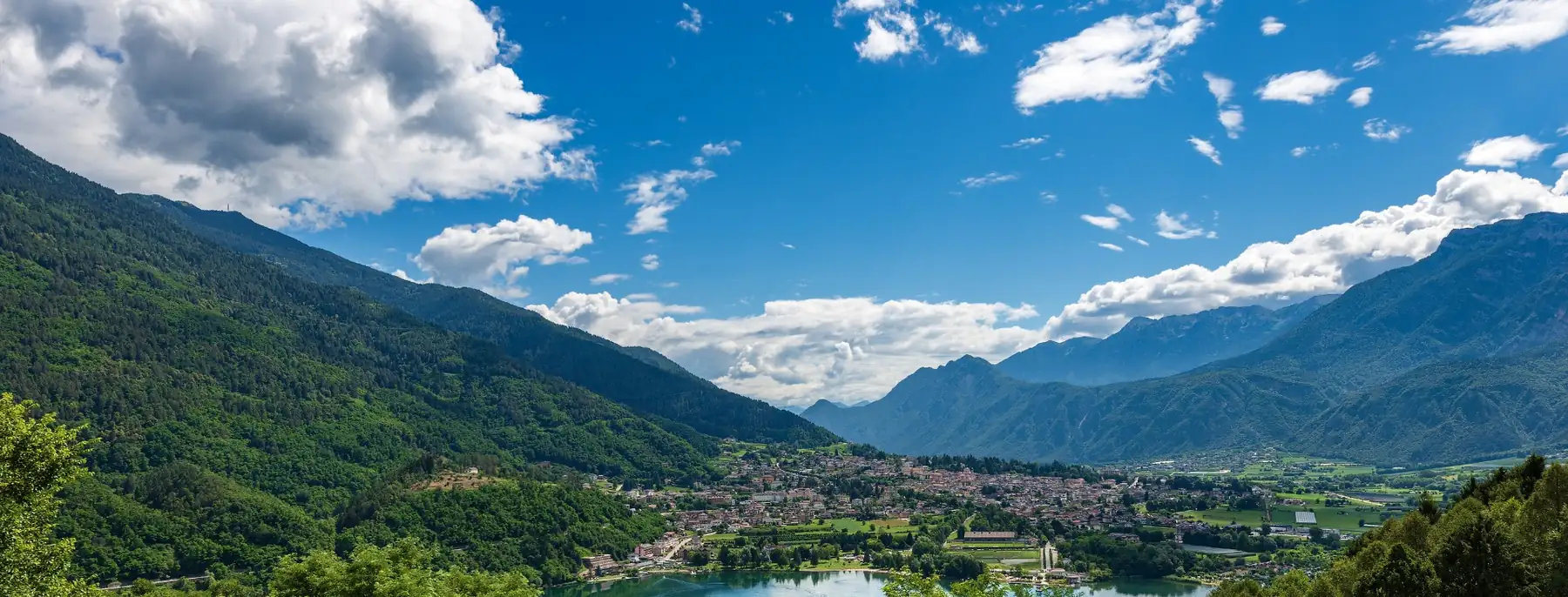 A lake in a green valley in Trentino, with mountains and cloud above