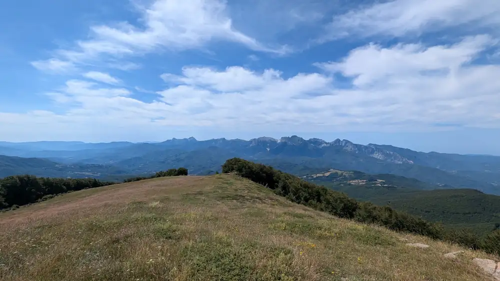 A grassy ridge above the hills of Lunigiana, with mountains on the horizon