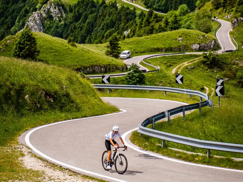 A cyclist on a hairpin bend on Monte Grappa, with more bends climbing the green slopes behind