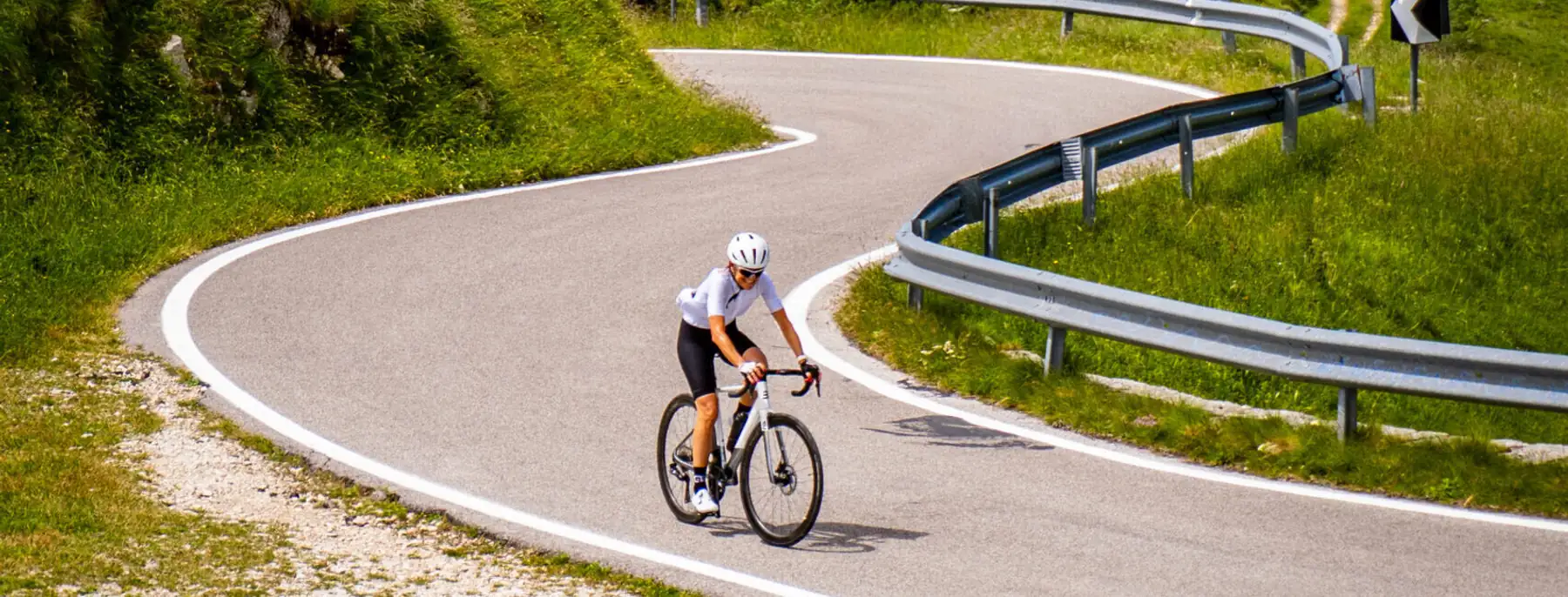 A cyclist on a hairpin bend on Monte Grappa, with more bends climbing the green slopes behind