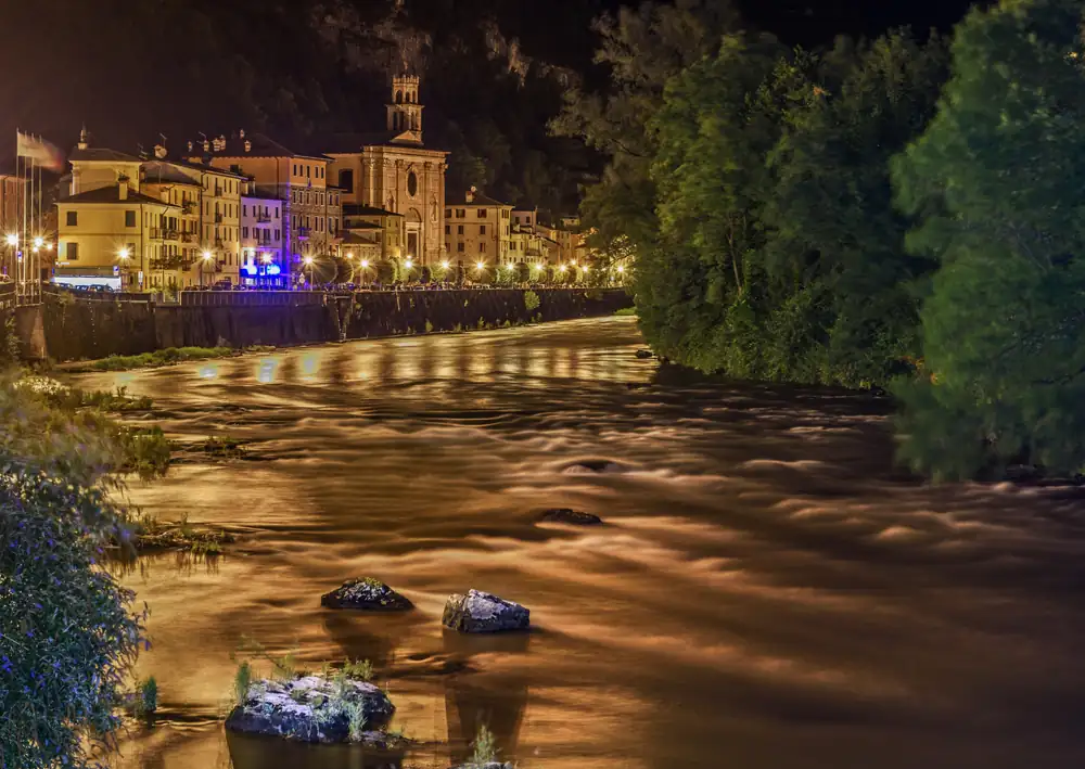 A river at night below a lit-up village