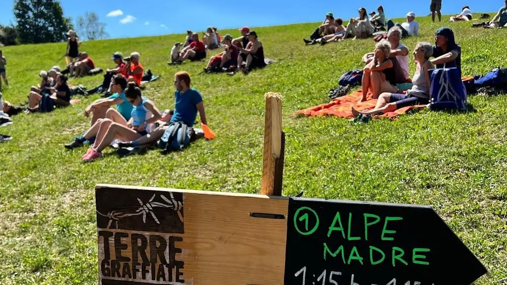 People sitting on a grassy slope on Monte Grappa beside a Terre Graffiate trail sign