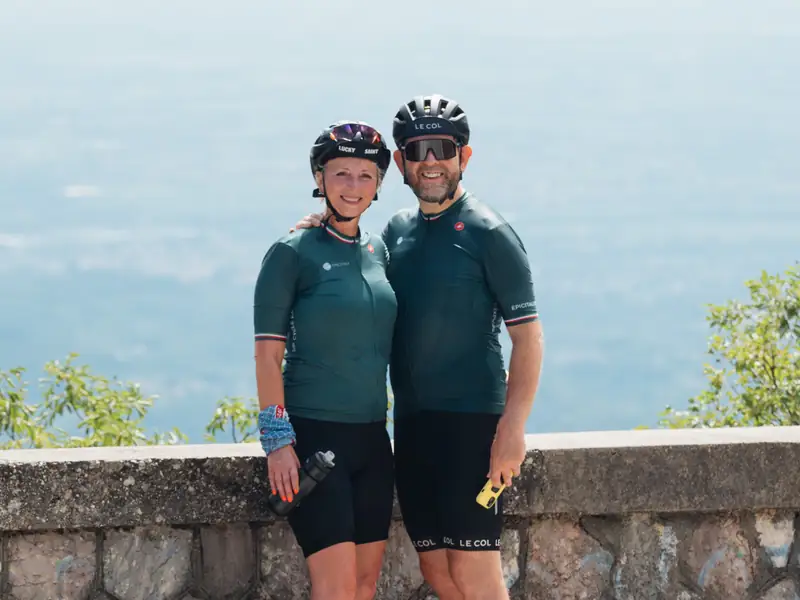 A couple in cycling kit standing at a stone wall high above the plain