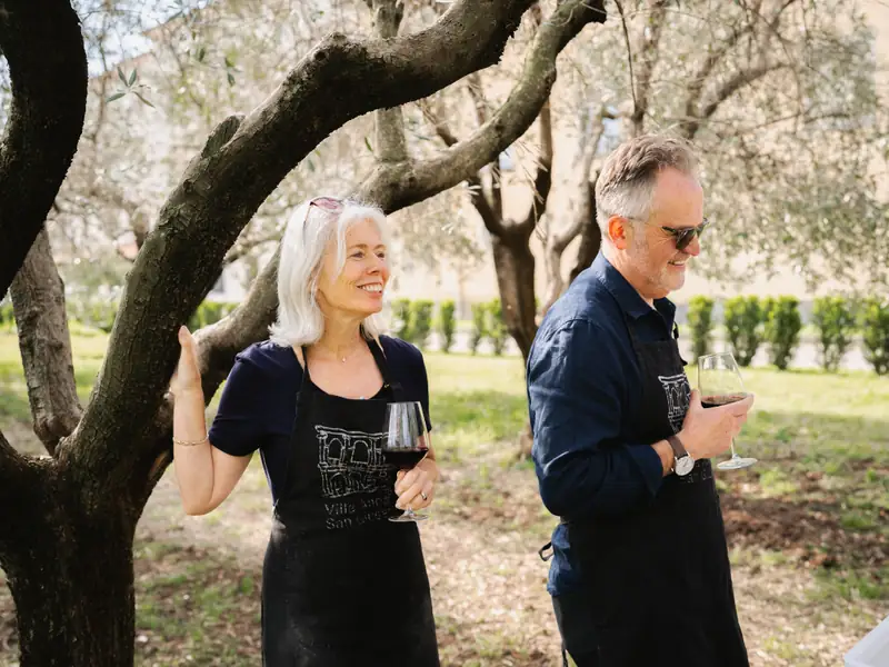 A couple holding glasses of wine among the olive trees